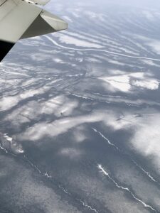 Blick aus dem Flugzeug auf eine gefrorene karge Landschaft mit nur wenig Schnee