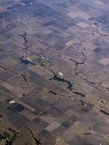Blick aus dem Flugzeug auf eine karge landwirtschaftlich geprägte Landschaft mit Windkraftanlagen im Hintergrund