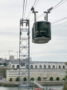 Zwei Seilbahnkabinen pendeln über das Hafenbecken. Interessant ist wie sie übereinander gleichzeitig den zentralen Mast passieren