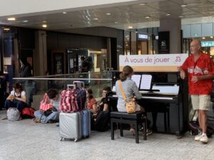 "Es ist an Ihnen zu spielen" steht über dem Klavier im Gare de Montparnasse. Ein Mann singt dazu.